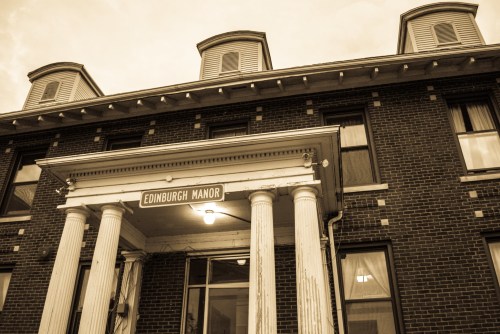 Historic building facade of Edinburgh Manor, featuring columns and a sign, with a cloudy sky in the background.