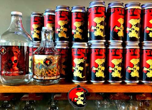 A display of custom-branded cans and bottles, featuring a spooky design, arranged on a wooden shelf.