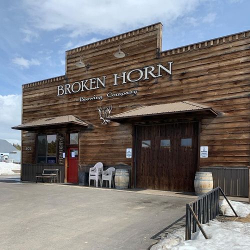 Exterior of Broken Horn Brewing Company, featuring a wooden facade, double doors, and outdoor seating.