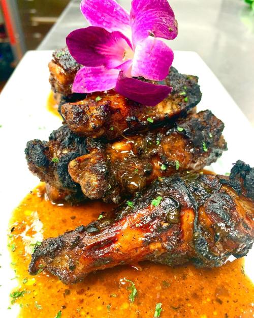 A plate of grilled chicken wings drizzled with sauce, garnished with a purple orchid and herbs.