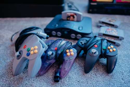 A collection of Nintendo 64 controllers and cartridges on a carpeted surface.
