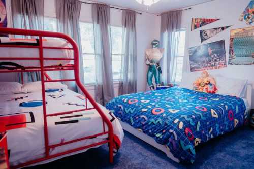 A colorful bedroom featuring a red bunk bed, a blue patterned bedspread, and playful decor on the walls.