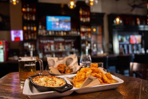 A wooden table with a beer, crispy potato chips, and a skillet of cheesy dip in a cozy bar setting.