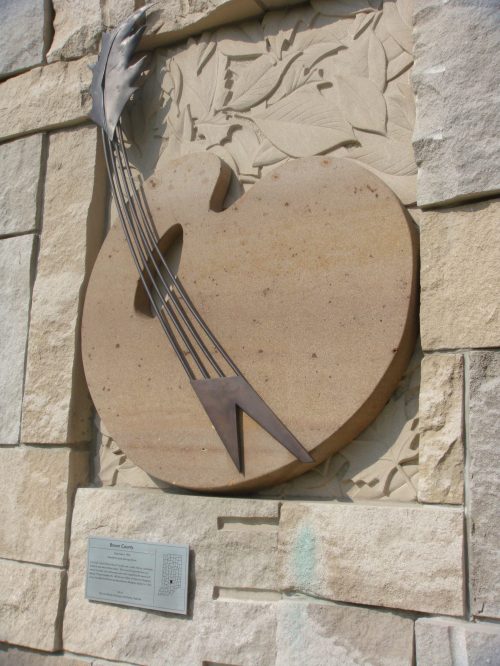 A stone wall sculpture featuring a guitar design with metal strings and a plaque below it.