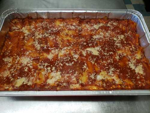 A large aluminum tray filled with baked pasta covered in marinara sauce and sprinkled with cheese.