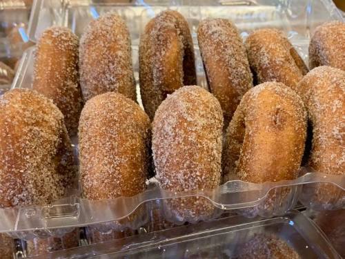 A close-up of freshly made, sugar-coated donuts arranged in a clear plastic container.