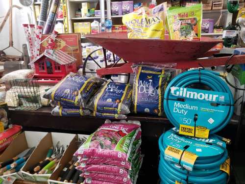 A display of gardening supplies, including soil, birdseed, and hoses, in a rustic shop setting.