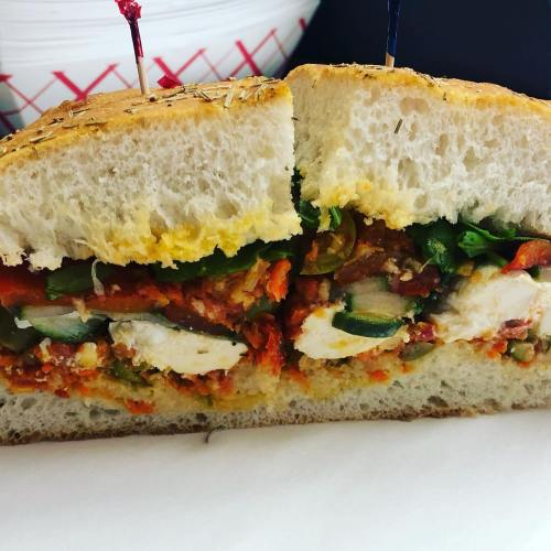 A cross-section of a sandwich filled with colorful vegetables, cheese, and herbs, served on a soft bread.