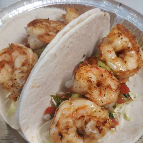 Two tacos filled with seasoned shrimp, lettuce, and diced tomatoes, served in a silver tray.
