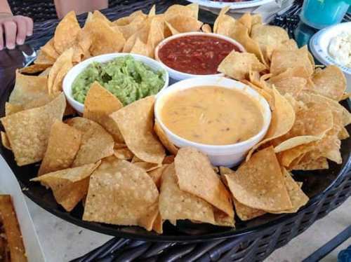 A large platter of tortilla chips surrounded by bowls of guacamole, salsa, and cheese dip.