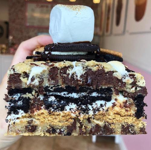 A layered dessert featuring chocolate, cookie, and marshmallow, topped with a toasted marshmallow and an Oreo.
