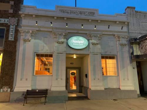 Exterior of Juniper Pizza Cafe, featuring a decorative facade and illuminated sign, at dusk.