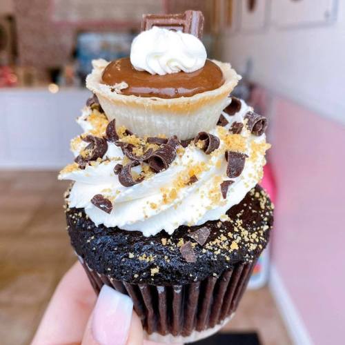 A decadent chocolate cupcake topped with whipped cream, caramel, chocolate shavings, and a mini pie crust.