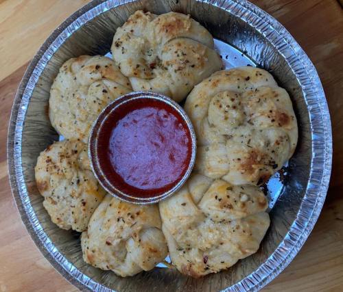 A silver tray with six garlic knots and a small cup of marinara sauce in the center.
