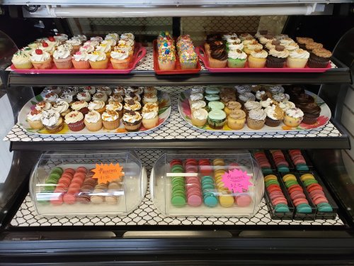 A display case filled with colorful cupcakes and macarons in various flavors, decorated with frosting and toppings.