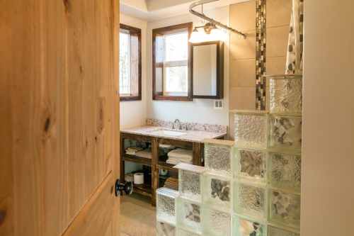 A modern bathroom with a wooden door, glass block wall, and a granite countertop with a mirror and sink.