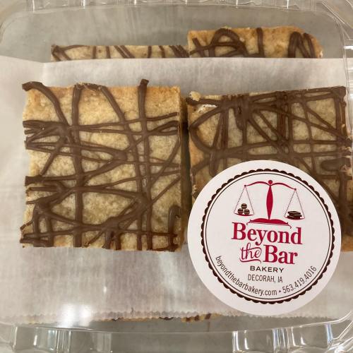 Three dessert bars drizzled with chocolate, placed in a clear container with a "Beyond the Bar Bakery" label.