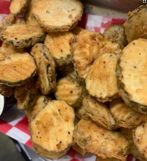 A close-up of crispy, golden-brown fried pickles served in a basket with a side of dipping sauce.