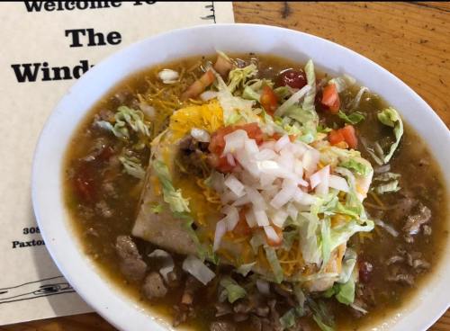 A hearty plate of enchiladas topped with cheese, lettuce, tomatoes, and onions, served with a side of green sauce.