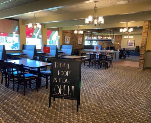 Interior of a restaurant with empty tables and a sign that says "Dining Room is now OPEN!" in a welcoming atmosphere.