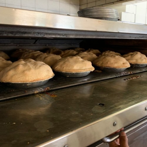 Freshly baked pies rising in a commercial oven, golden crusts in metal pans.