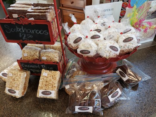 A display of various treats, including Scotcharoos, caramel rice crispies, and packaged snacks on a red pedestal.