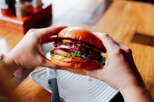 A person holds a delicious burger with lettuce, onion, and a juicy patty, ready to take a bite.