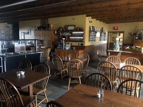 A cozy restaurant interior with wooden tables, chairs, and a buffet area, featuring warm lighting and rustic decor.