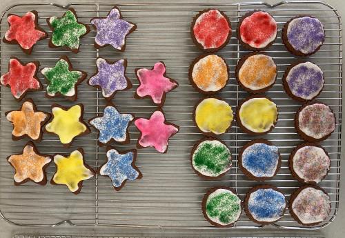 A cooling rack with colorful star and round cookies, decorated with vibrant icing and sprinkles.