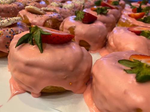 Close-up of pink-glazed donuts topped with fresh strawberries and colorful sprinkles.