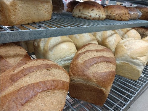Freshly baked loaves of bread on a metal rack, including whole grain and white varieties.