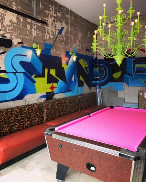 A vibrant room featuring a pink pool table, leopard-print seating, and colorful graffiti on the wall.
