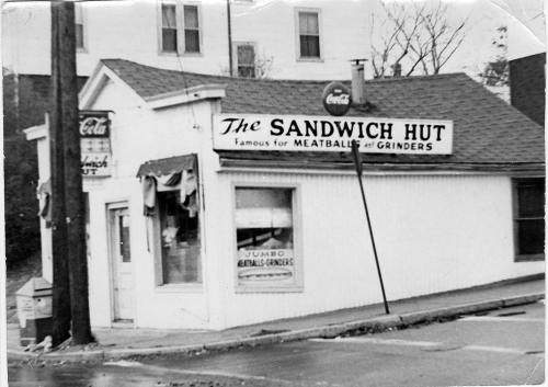 Black and white photo of "The Sandwich Hut," a small eatery known for meatballs and grinders, with vintage signage.