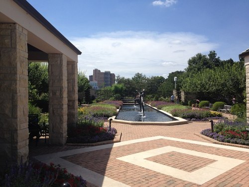 A serene garden with a water feature, surrounded by colorful flowers and greenery, under a clear blue sky.