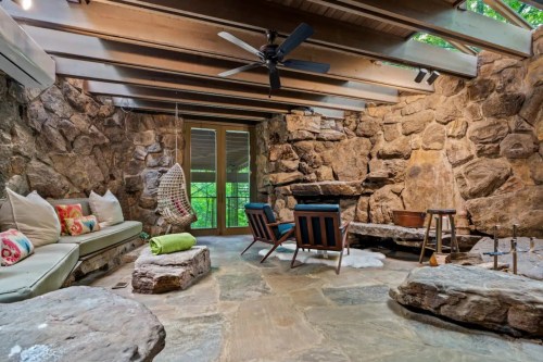 Cozy interior with stone walls, wooden beams, a fireplace, and seating area featuring a hammock and colorful cushions.