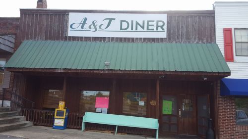 Exterior of A&T Diner featuring a green metal roof, wooden facade, and a bench outside.
