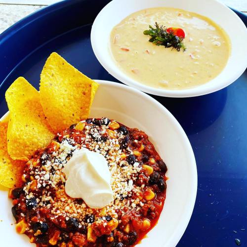 A plate of chili topped with sour cream and cheese, served with tortilla chips, alongside a bowl of creamy soup.