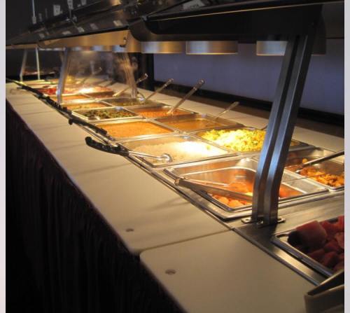A buffet line with various dishes displayed in metal trays under warm lights.