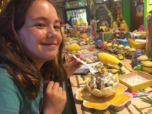 A smiling girl holds a dessert topped with whipped cream and sprinkles, surrounded by colorful decorations and toys.