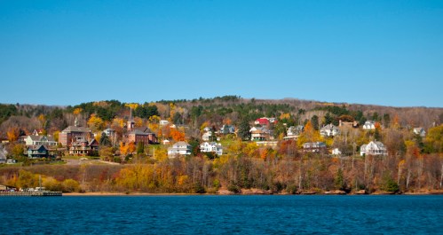 A scenic view of a hillside with colorful autumn trees and charming houses overlooking a calm lake.