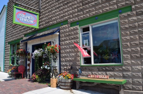A charming storefront with colorful flowers, a sign reading "Stone's Throw," and a welcoming open window.