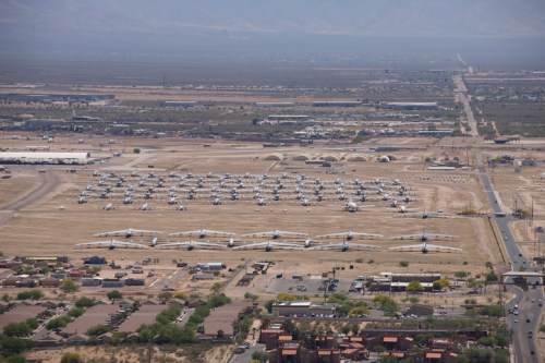 Aerial view of an aircraft storage facility with numerous planes parked on a dry landscape near a road and buildings.