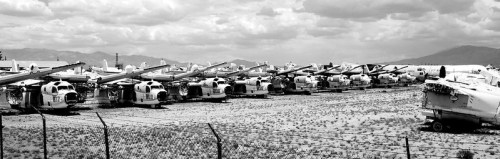 A row of abandoned helicopters parked in a dusty field under a cloudy sky.