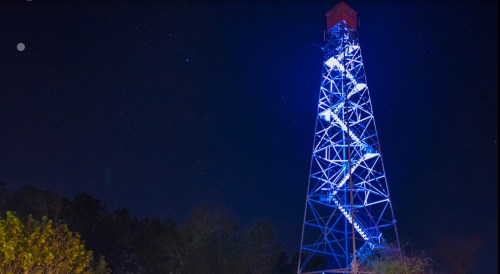 A tall, illuminated tower against a starry night sky, with blue lights highlighting its structure.