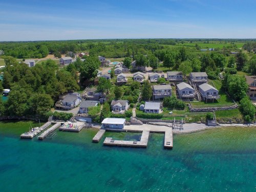 Aerial view of a lakeside community with houses, docks, and lush greenery under a clear blue sky.