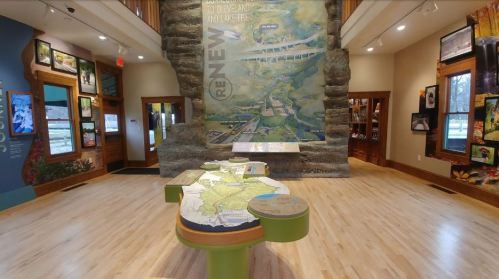 Interior view of a visitor center featuring a large mural and a 3D map display on a wooden floor.