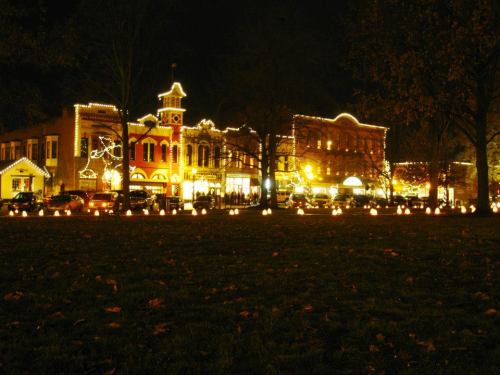 A festive street scene at night, adorned with bright lights and lanterns, surrounded by trees and autumn leaves.