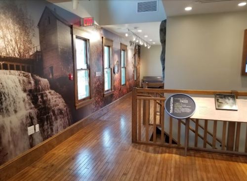 Interior view of a museum hallway featuring a waterfall mural, wooden flooring, and informational displays.