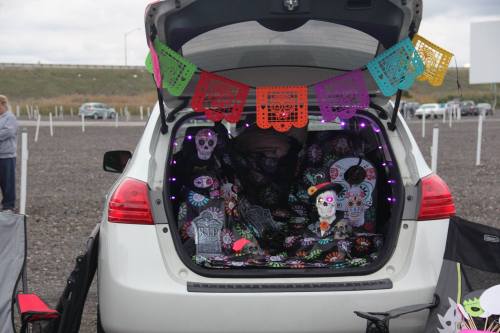 A decorated car trunk with colorful papel picado, skulls, and lights, set up for a festive celebration.