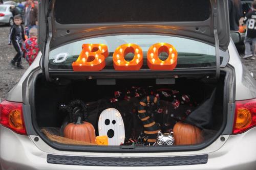 Trunk decorated for Halloween with "BOO" lights, pumpkins, a ghost, and a black cat, set in a festive atmosphere.